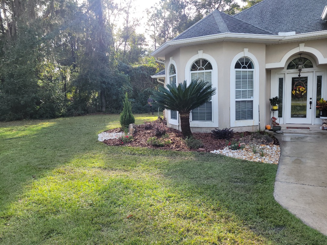 Well-maintained front landscape with palm and evergreen shrubs, decorative white rocks, mulch, and a curved sidewalk entrance.