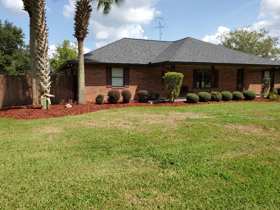 Large backyard landscape with fresh dark brown and light mulch under trees, bordered with ornamental shrubs and garden beds.