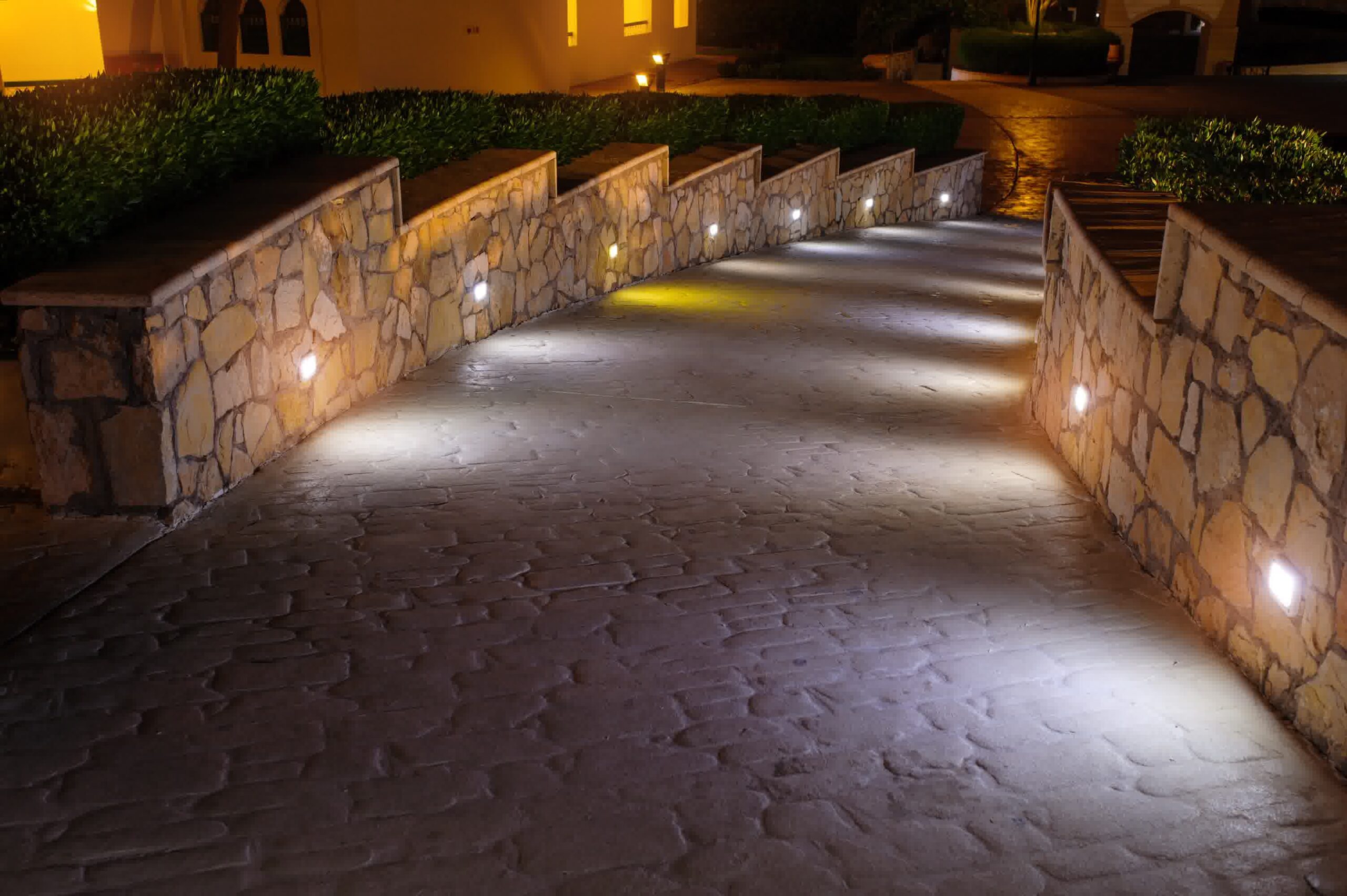 Curved stone retaining wall with built-in LED lights illuminates decorative concrete driveway for safety and modern landscape design.